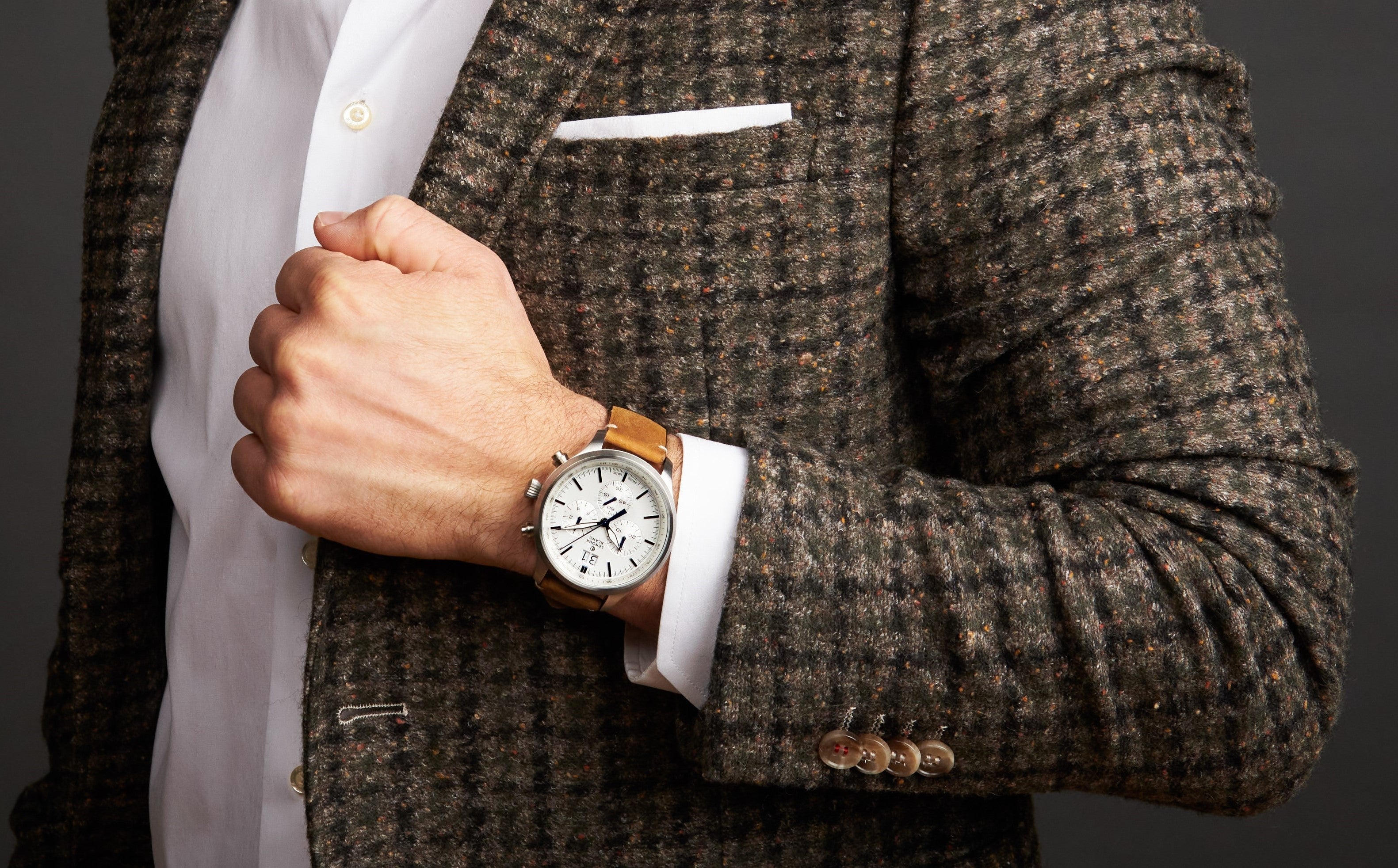 Elegante Armbanduhr am Handgelenk zu einem dunklen Anzug, detailnah fotografiert